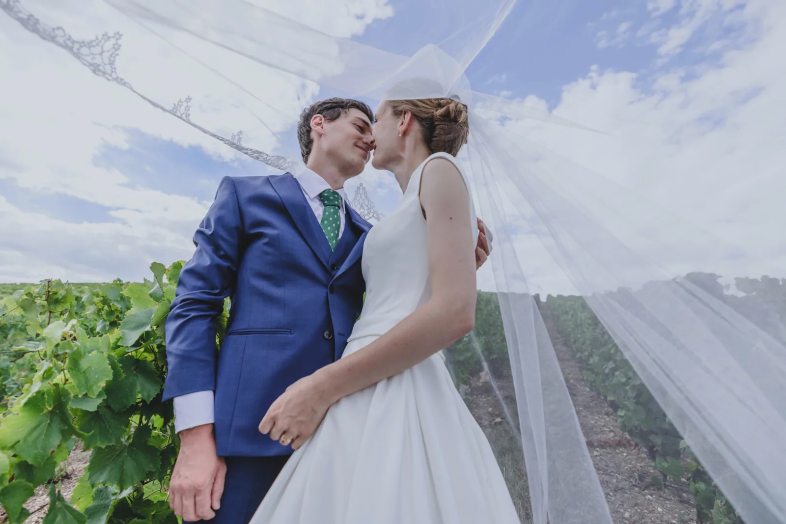 Baiser des mariés sous le voile, le marié en costume bleu et cravate verte