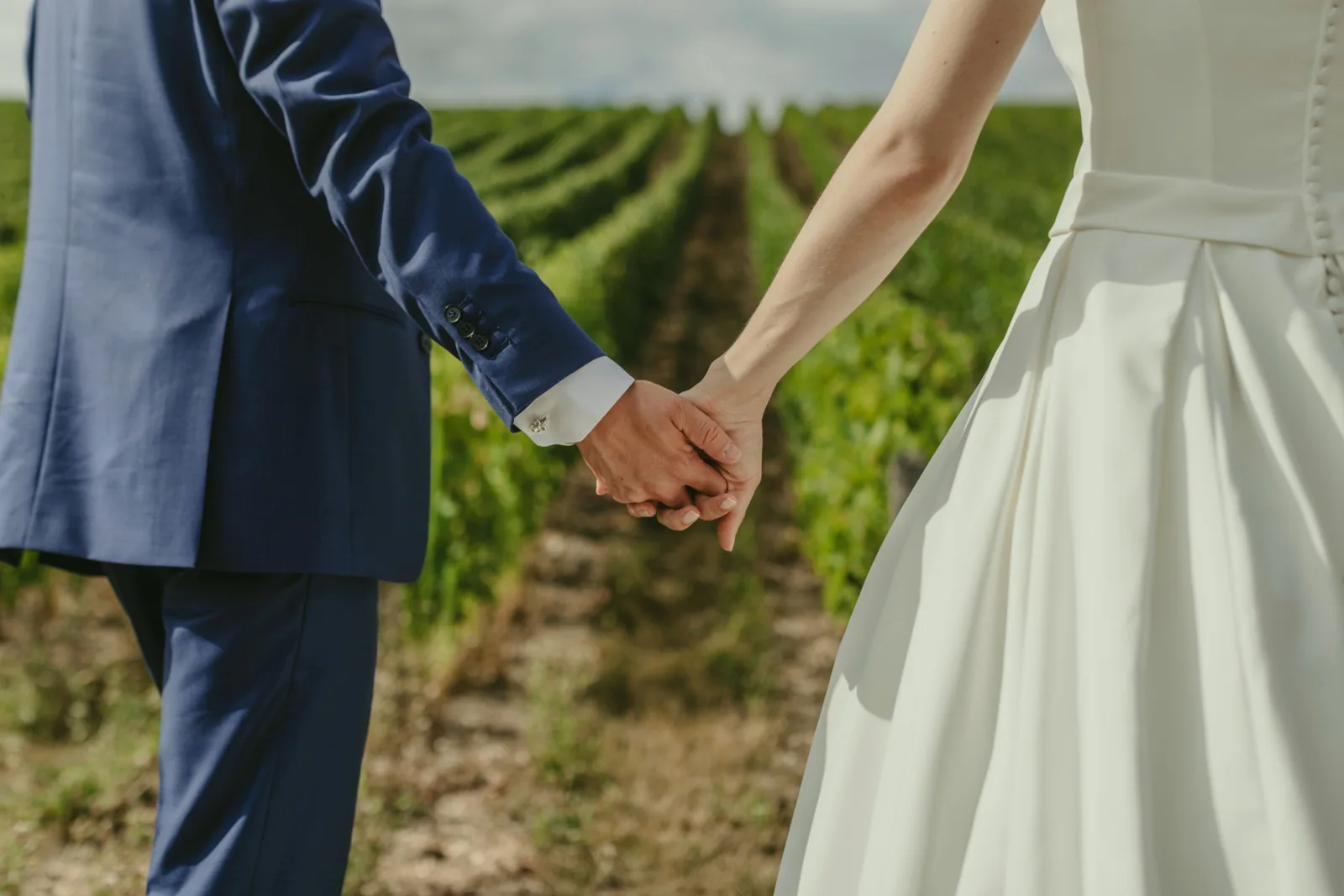 Mains des mariés qui se rejoignent devant un rang de vignes