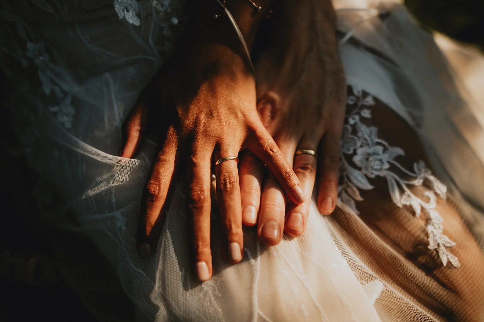 Mains des mariés superposées, alliances et dentelle de la robe