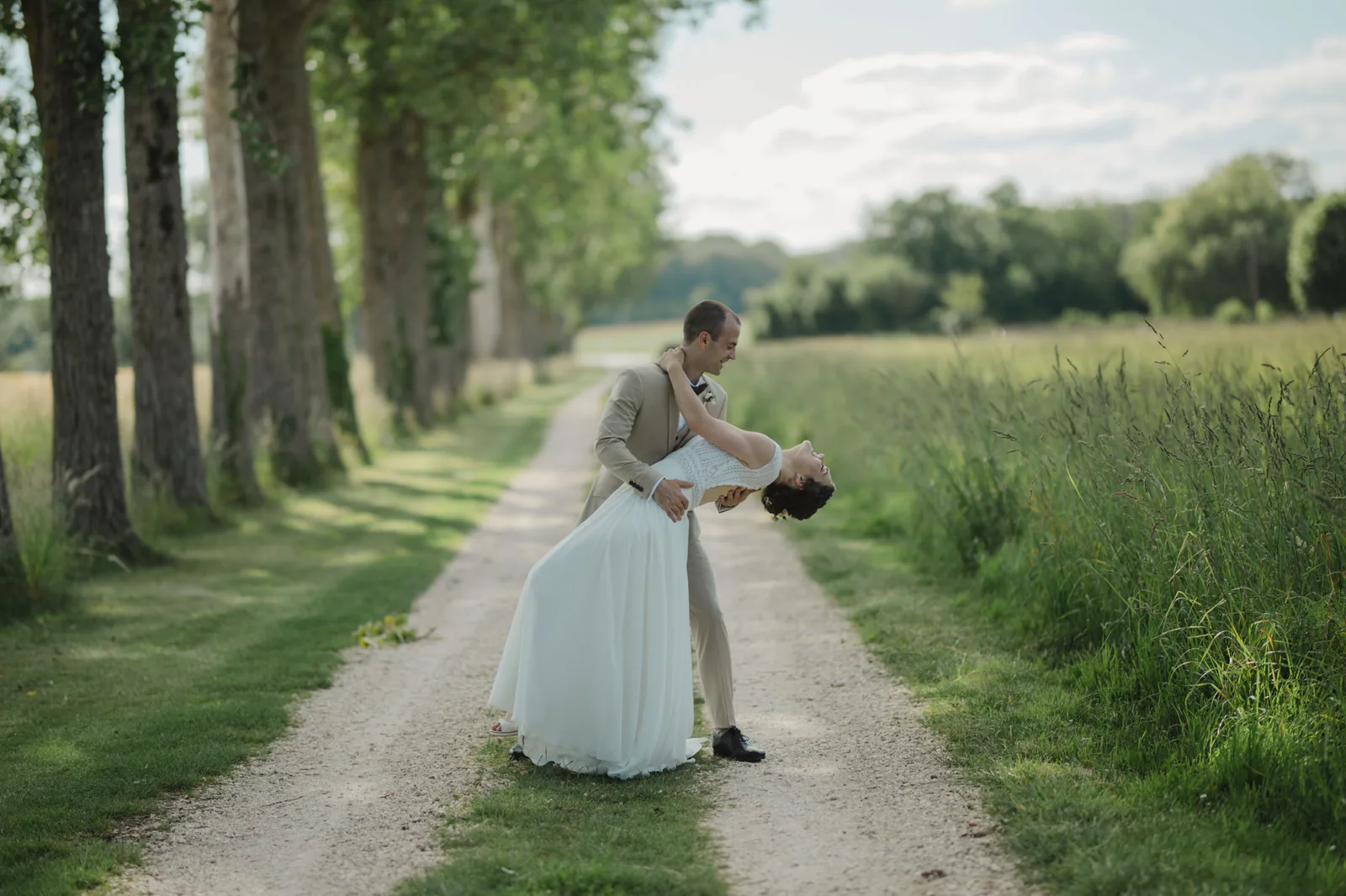 Le marié soulève la mariée dans une allée de campagne bordée d'arbres