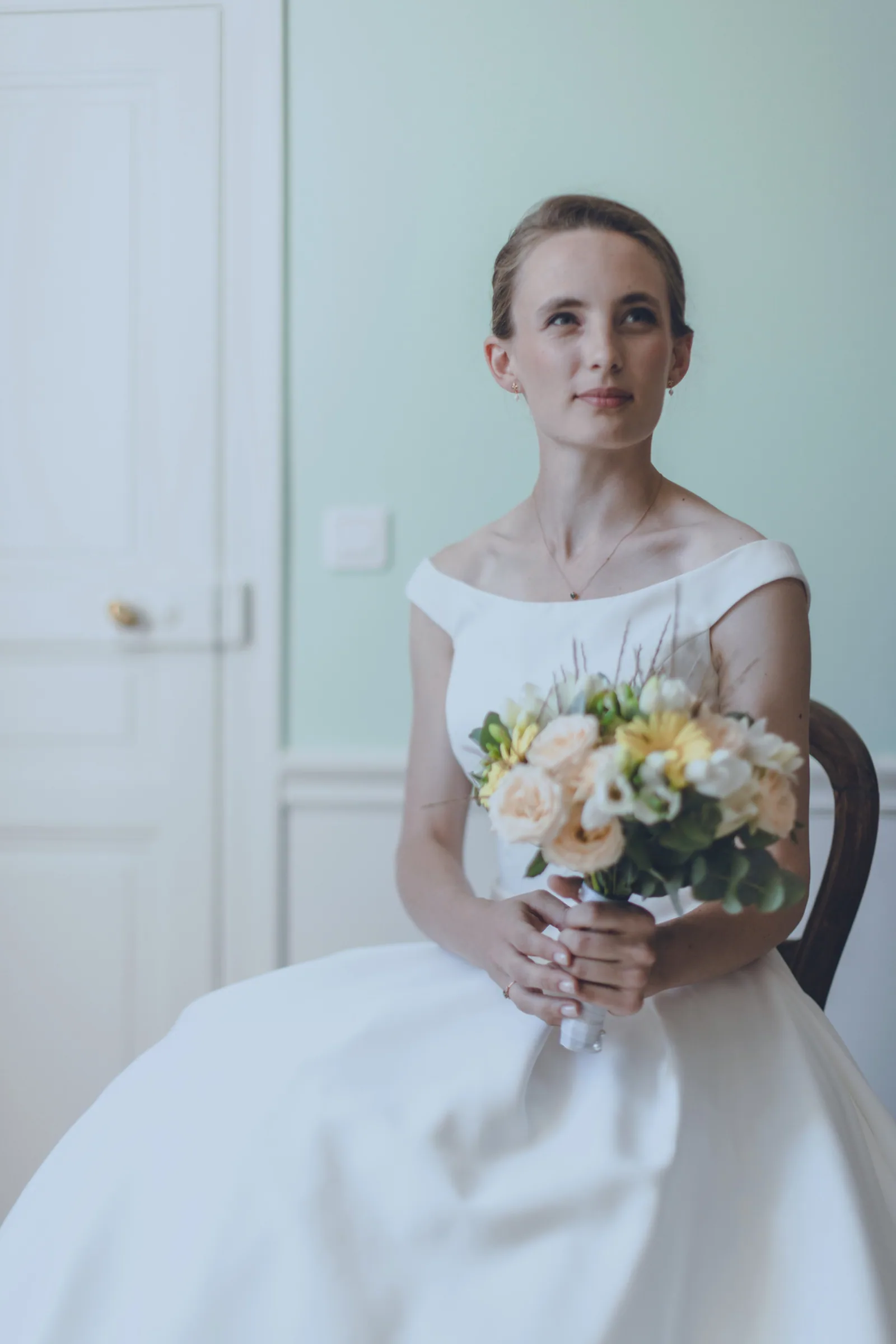 Portrait de mariée en robe épaules dénudées tenant son bouquet dans une lumière naturelle douce