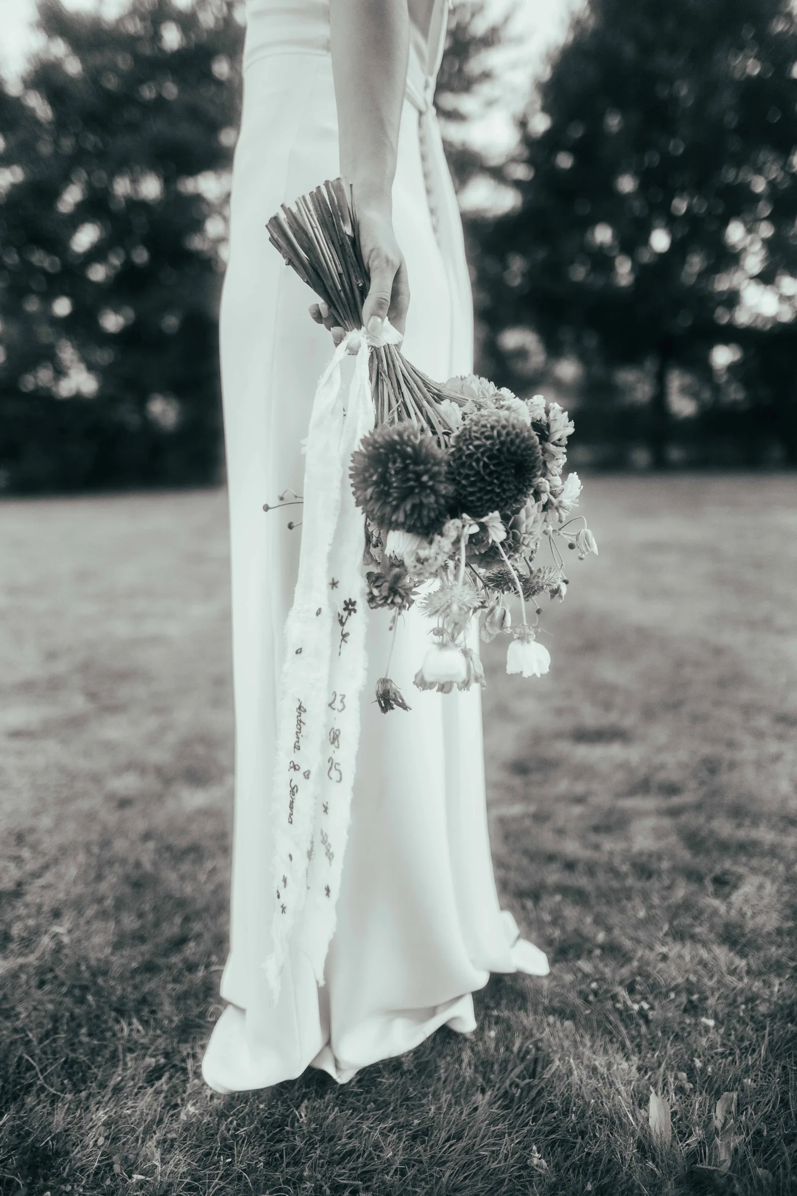 Robe de mariée suspendue à un arbre avec le bouquet, en noir et blanc