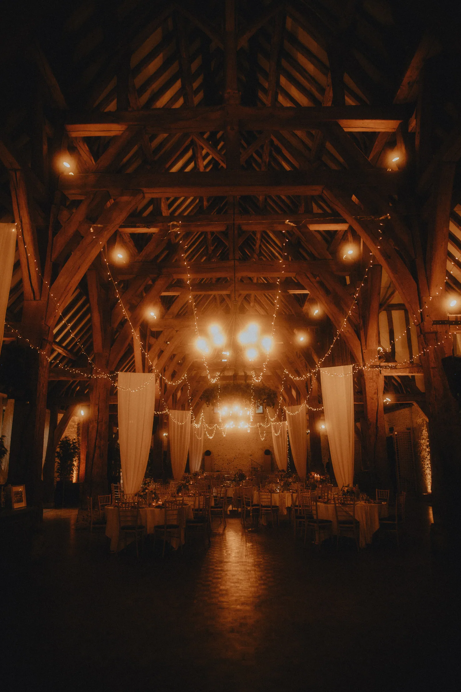 Salle de réception sous charpente en bois avec lustres et guirlandes